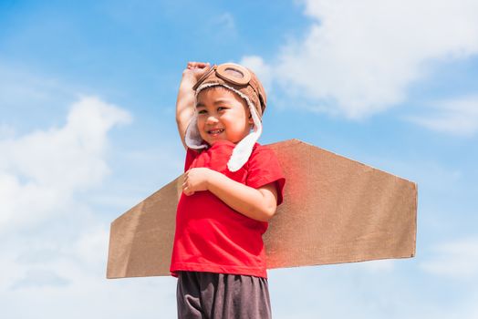 Happy Asian funny child or kid little boy smile wear pilot hat and goggles play toy cardboard airplane wing flying raises hand up against summer blue sky cloud background, Startup freedom concept