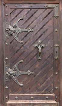 Ancient antique wooden doors with wrought iron loops, massive forged door handle and cross bars.
