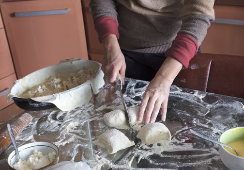 Female hands cut the dough on a glass table with a knife to make a cake with cottage cheese.