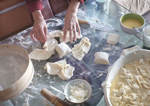 Female hands roll the dough on a glass table to make a cake with cottage cheese.
