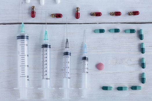 Medical syringes of various capacities, capsules, pills lie vertically on a white roughly painted wooden table.