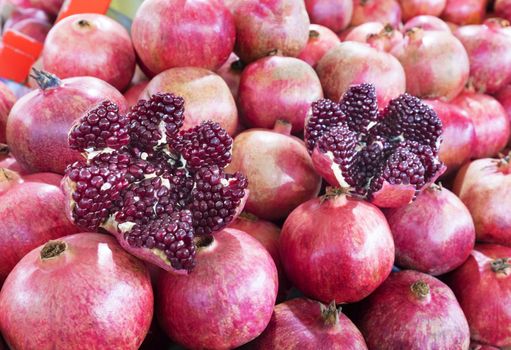 Ripe and red fruit pomegranate and divided into four parts, against the background of pomegranate fruit lined in rows