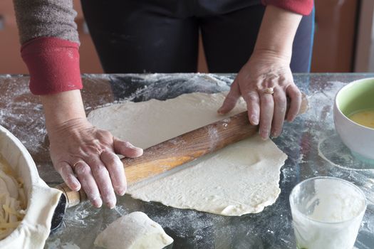 Female hands roll the dough on a glass table to make a cake with cottage cheese.