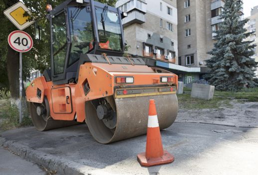 Orange road cone protect the working area for heavy vibrating compactor on a city street
