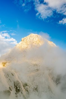 Sun Illuminated Mangart Mountains Peak in Clouds and Fog.