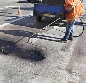 The road maintenance worker sprays the bitumen mixture onto the cleaned area for better adhesion to the new asphalt