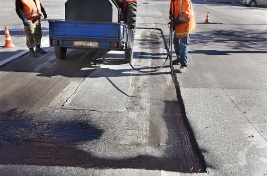 The road maintenance worker sprays the bitumen mixture onto the cleaned area for better adhesion to the new asphalt