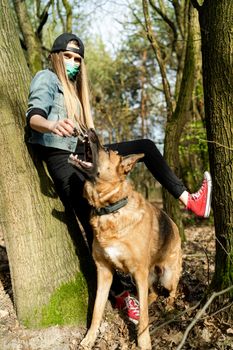 Young Casual Woman Play with Dog Outdoor in Park while Wearing Face Mask. Coronavirus Pandemic New Normal.