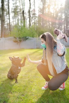 Young Woman Wearing Face Mask Play With Cute Dog in Home Garden or Park. Coronavirus Pandemic New Normal.