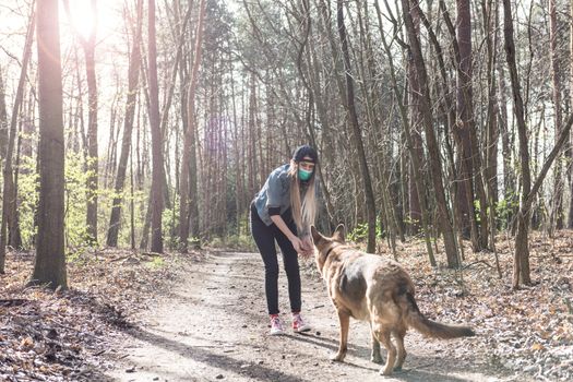 Young Casual Woman Play with Dog Outdoor in Park while Wearing Face Mask. Coronavirus Pandemic New Normal.