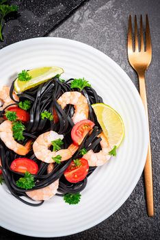 Black Pasta - Squid Ink, with Prawns, Seafood,Lemon and Tomatoes in White Bowl on  Dark Background. Top view.