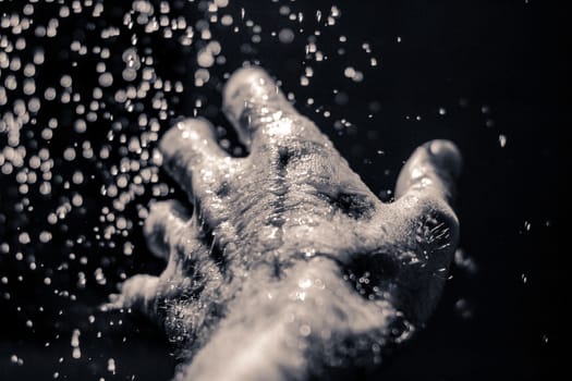 Photograph of an open human hand under water drops