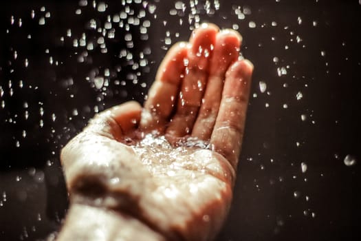 Photograph of an open human hand under water drops