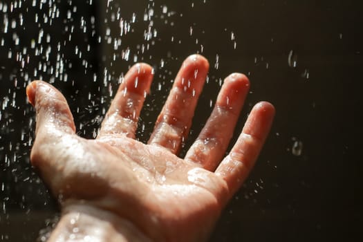 Photograph of an open human hand under water drops