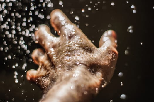 Photograph of an open human hand under water drops