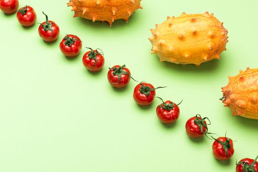 Red Tomatoes and Yellow Kiwano Flat Lay Pattern. Green Background with Raw Vegetables.