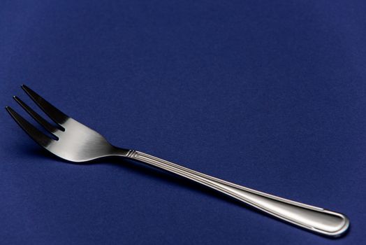 Single One Stainless Steel Fork on Blue Background. Detail Close Up View.