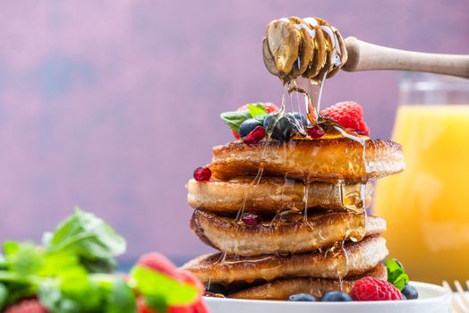 Pouring Honey on Pancakes Stack Topped with fresh Fruits. Shrove Tuesday Breakfast.