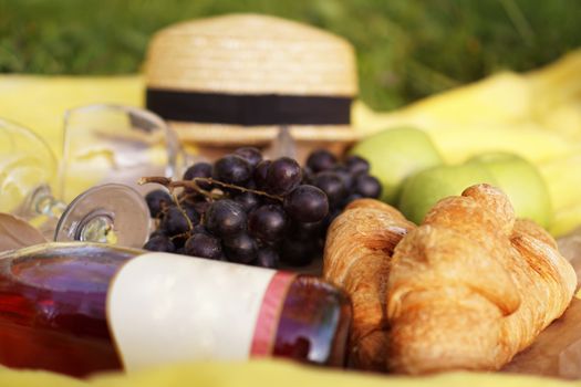 Picnic on the grass with croissant, pink wine, straw hat, grape on yellow plaid and green grass. Summer time