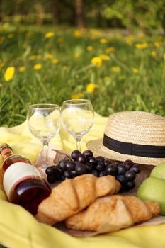 Picnic on the grass with croissant, pink wine, straw hat, grape on yellow plaid and green grass. Summer time - vertical photo