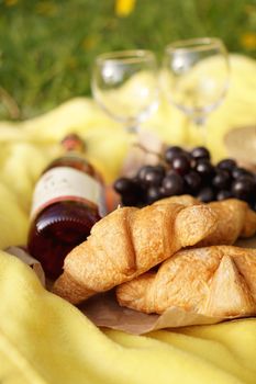 Picnic on the grass with croissant, pink wine, straw hat, grape on yellow plaid and green grass. Summer time - vertical photo