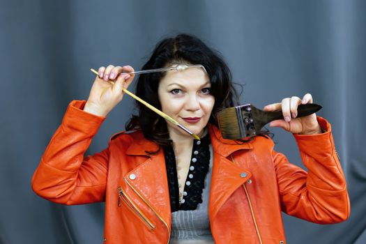 Portrait of a beautiful fashionable middle-aged woman in a bright orange leather jacket, posing on a dark gray background