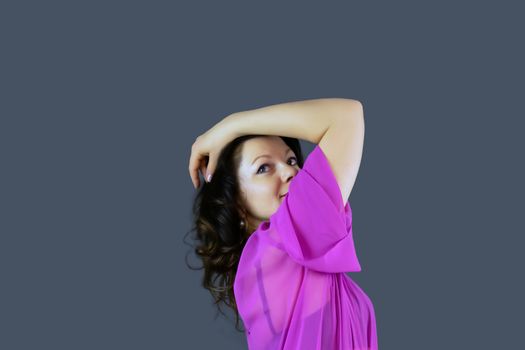 Portrait of a beautiful fashionable middle-aged woman in a bright pink semi-transparent long dress, posing on a dark gray background. The concept of preserving youth at any age.