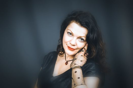 Portrait of a beautiful fashionable middle-aged woman in a black dress, posing on a dark gray background. Vintage style. The concept of preserving youth at any age.