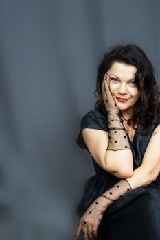 Portrait of a beautiful fashionable middle-aged woman in a bright pink semi-transparent long dress, posing on a dark gray background. The concept of preserving youth at any age.