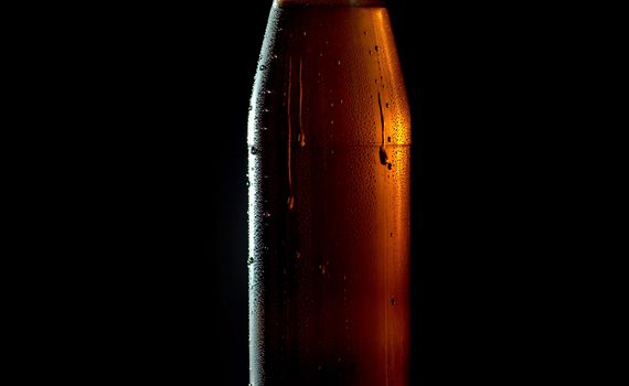 Close up cold beer in a misted glass bottle on a black background. Drops of water flowing down. A ray of light beautifully illuminates it. Craft beer closeup