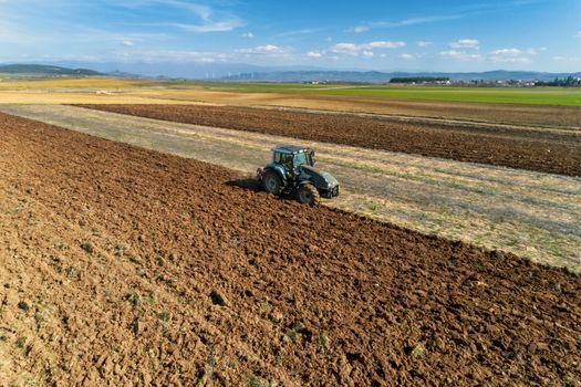 Aerial drone shot of a farmer in tractor seeding, sowing agricultural crops at field in the fertile farm fields of Kilkis in North Greece