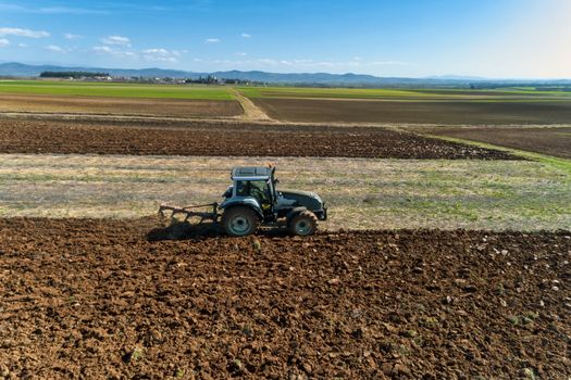 Aerial drone shot of a farmer in tractor seeding, sowing agricultural crops at field in the fertile farm fields of Kilkis in North Greece