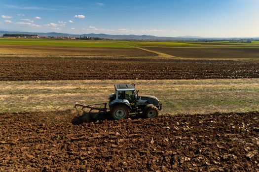 Aerial drone shot of a farmer in tractor seeding, sowing agricultural crops at field in the fertile farm fields of Kilkis in North Greece