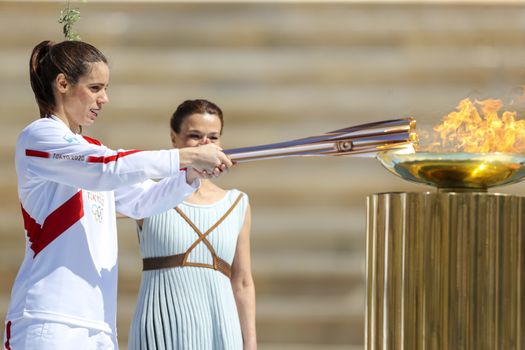 Athens, Greece - March 19, 2020: Olympic Flame handover ceremony for the Tokyo 2020 Summer Olympic Games at the Panathenaic  Stadium. Greek athlet K. Stefanidi (L) is seen lighting the cauldron