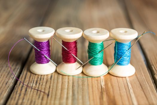 Spools of thread with needles on wooden background. Old sewing accessories. colored threads