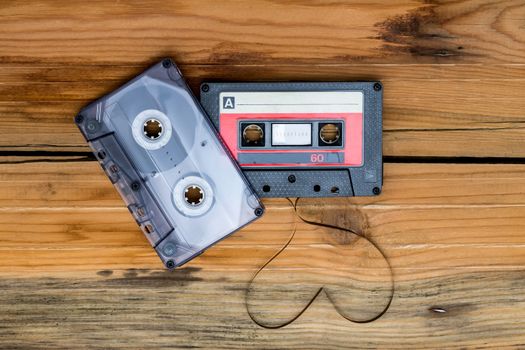 Vintage audio cassette with loose tape shaping one heart on a wooden background.