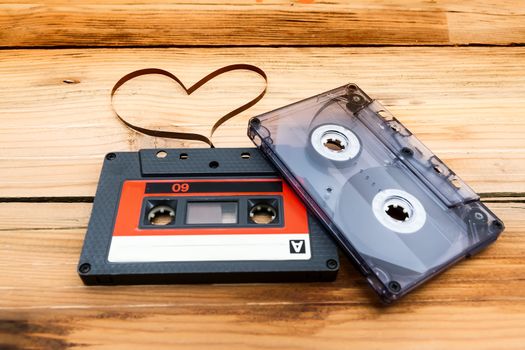 Vintage audio cassette with loose tape shaping one heart on a wooden background.