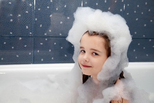 portrait of little girl sitting in a bath with soap suds