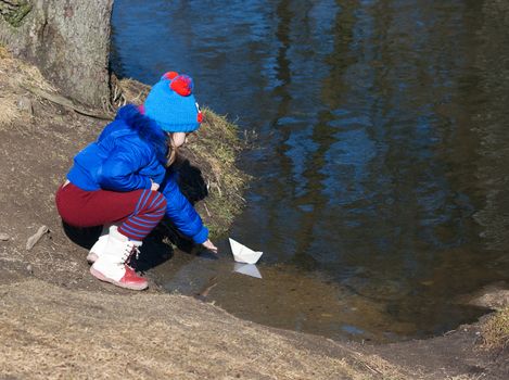 little girl playing with paper boat on the river on sunny spring day