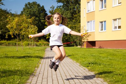 little girl in white shirt and black shorts jumping rope outside