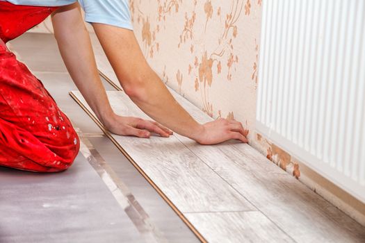 young handyman installing wooden floor in new house, hands closeup