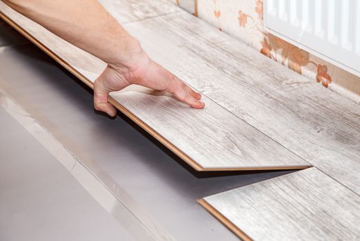 young handyman installing wooden floor in new house, hands closeup