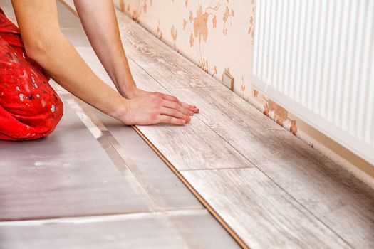 young handyman installing wooden floor in new house, hands closeup