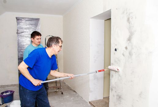 elderly worker painting wall with background glue for a wallpaper with his son