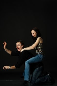 funny young couple play in studio on black background