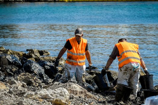 Salamis, Athens, Greece - Sept 13, 2017: Workers try to clean up oil that has washed ashore, on a beach of Salamis island near Athens, after an old tanker sank close to Salamis island