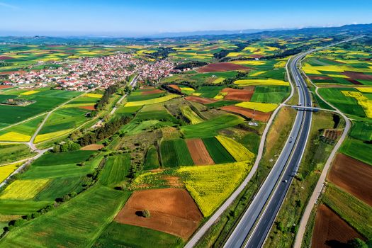 Aerial view of road passing through a rural landscape with blooming rape in northern Greece