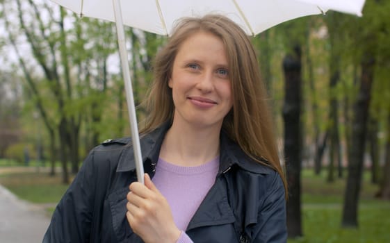 Beautiful smiling woman with umbrella under rain in the park. Outdoors portrait of young blond woman. Real people.