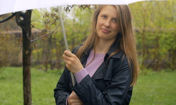 Beautiful smiling woman with umbrella under rain in the park. Outdoors portrait of young blond woman. Real people.