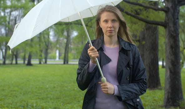 Rainy day in the park. Attractive woman walking with umbrella under rain. Outdoors female portrait. Real people